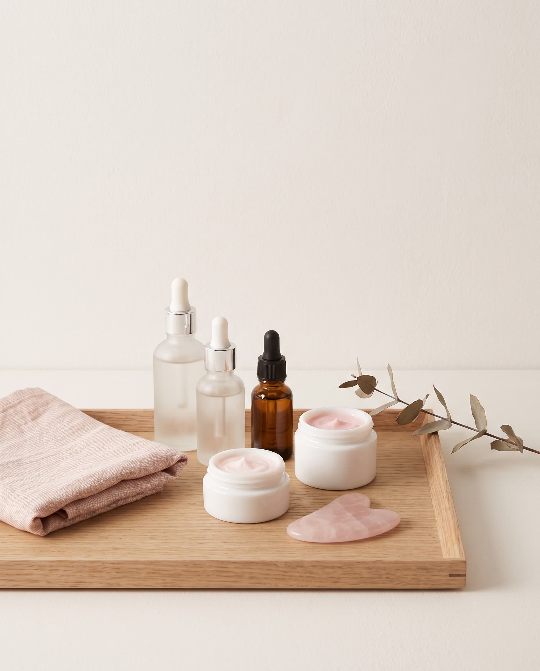 Oak tray with serums, a soft pink cream and a rose quartz gua sha stone